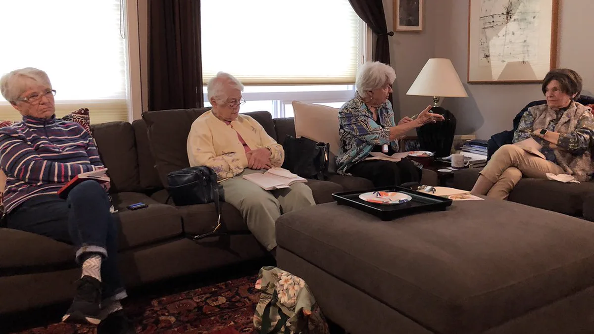 Small Reading Group Discussing a Novel on a Sofa at Home Four older readers on sofas in a lamp-lit living room, books on their laps, during relaxed book club discussion questions