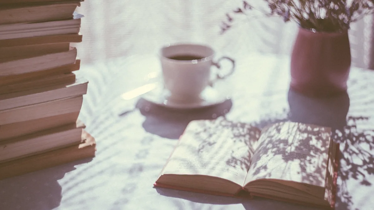 Open Book, Stacked Books and a Cup of Tea by the Window An open book beside a stack of books and a cup of tea on a sunlit table, ready for reading the first book club pick