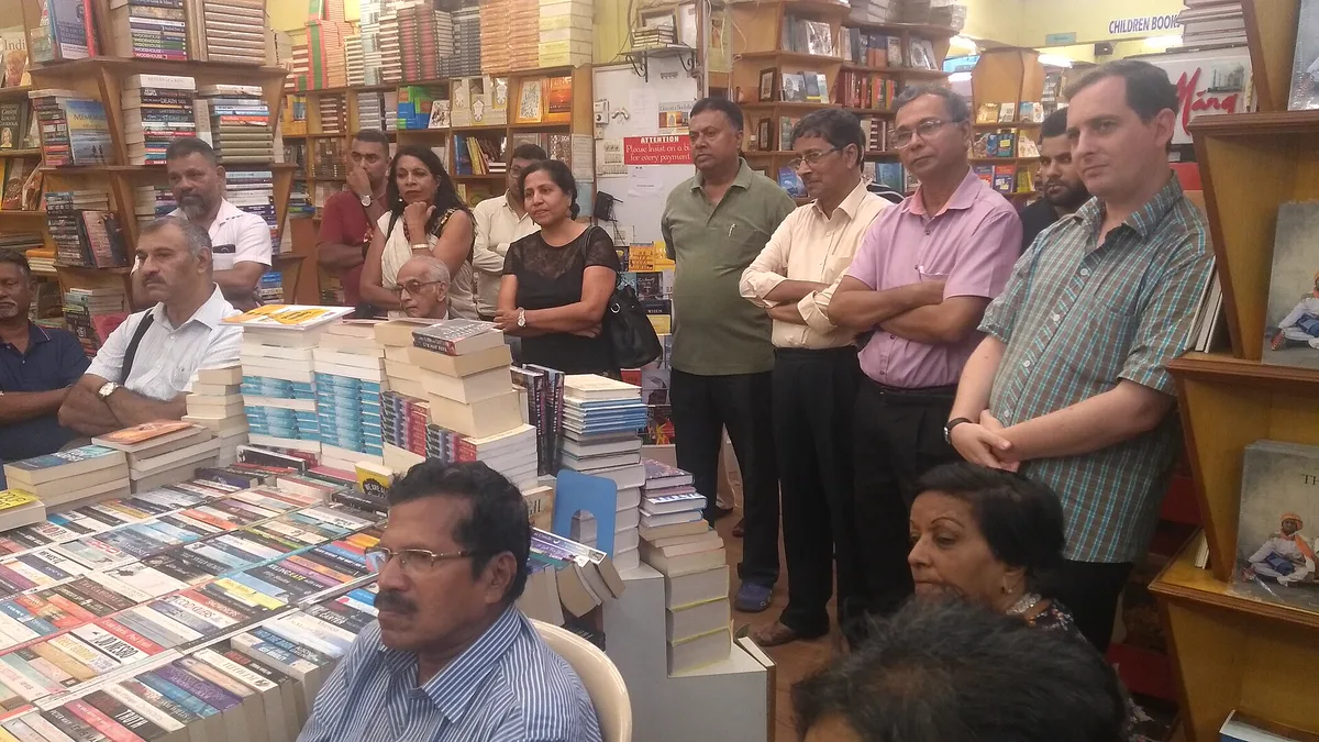 Readers Gathered Among Bookshop Shelves for a Book Club Meeting A group of adult readers sitting and standing between crowded bookshop shelves and stacked paperbacks at a book club meeting