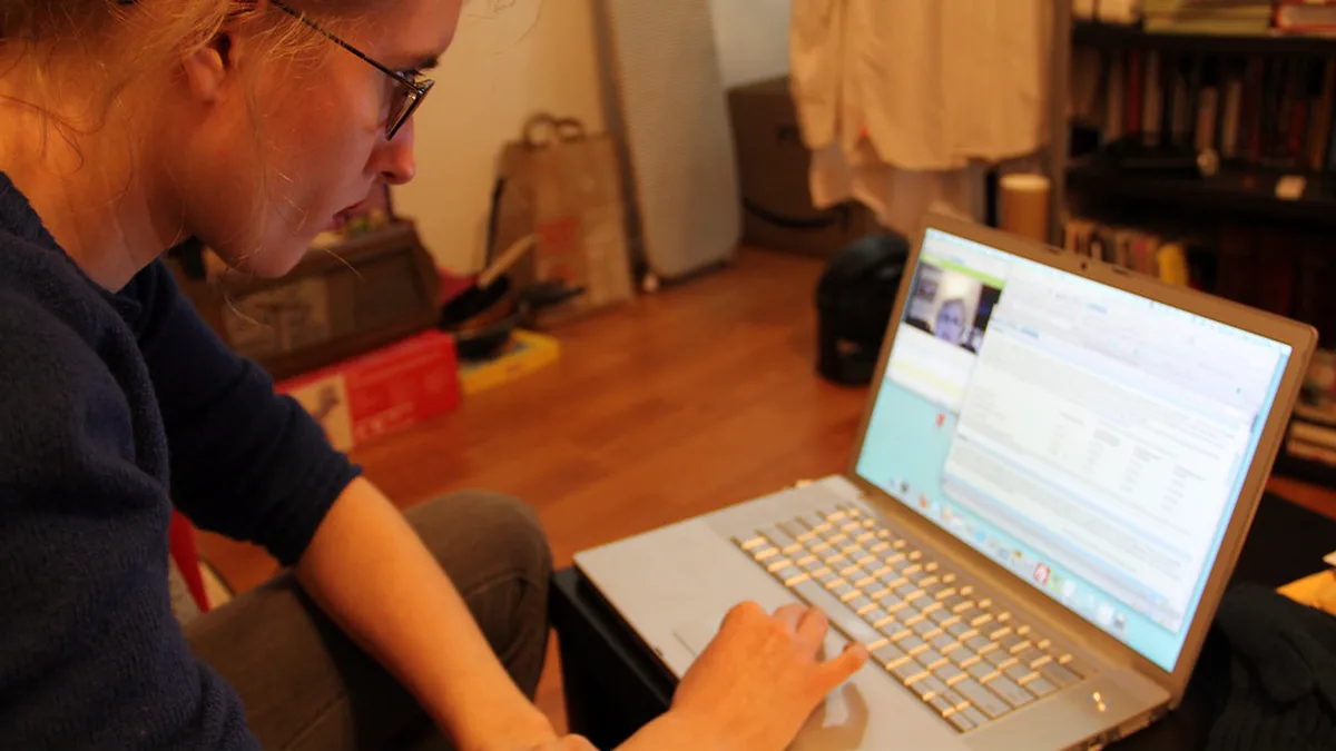 Reader Joining a Video Call From Home on a Laptop A woman at home typing on a laptop during a video chat, with bookshelves behind her, the setup for an online book club