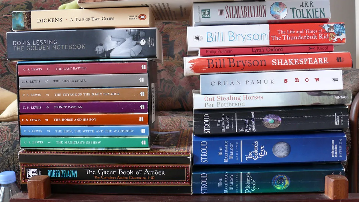 To-Read and Finished Book Stacks Two stacks of paperbacks and hardcovers on a sofa arm, unread books beside finished ones, a visual check on yearly reading goals