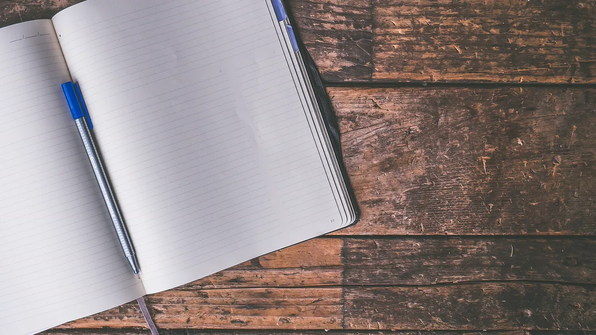 Blank Notebook and Pen Ready for a New Reading Journal Open blank notebook with a blue pen on a dark wooden table, ready for reading journal ideas like a book log and quote page