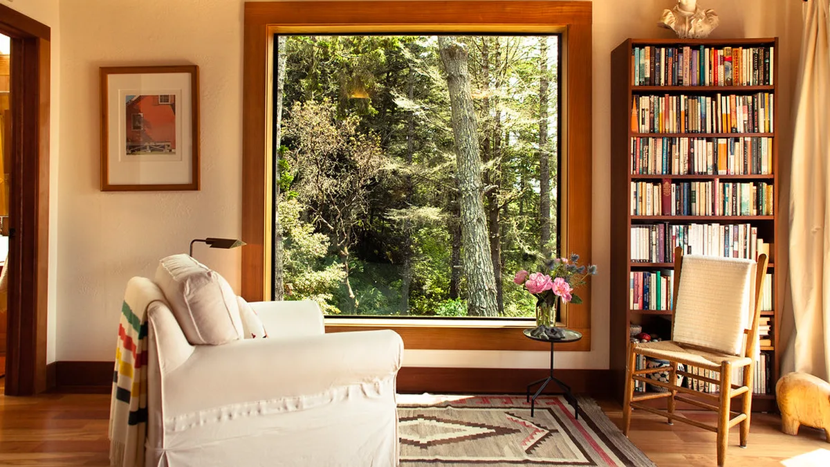Reading nook ideas in a living room: white slipcovered armchair with a swing arm lamp beside a large window and a tall bookshelf