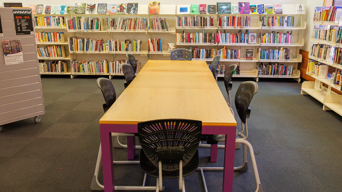 Long wooden reading table with black chairs in front of nonfiction shelves at Waiuku Library, a calm place to slow down