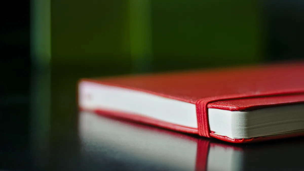 Red Notebook for a Handwritten Reading List A closed red hardcover notebook with an elastic band on a dark glossy table, the kind of notebook used for a paper reading list